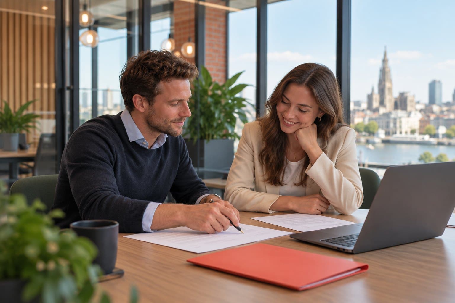 Een recruiter en een adviseur overlopen samen documenten aan een tafel, met zicht op Antwerpen