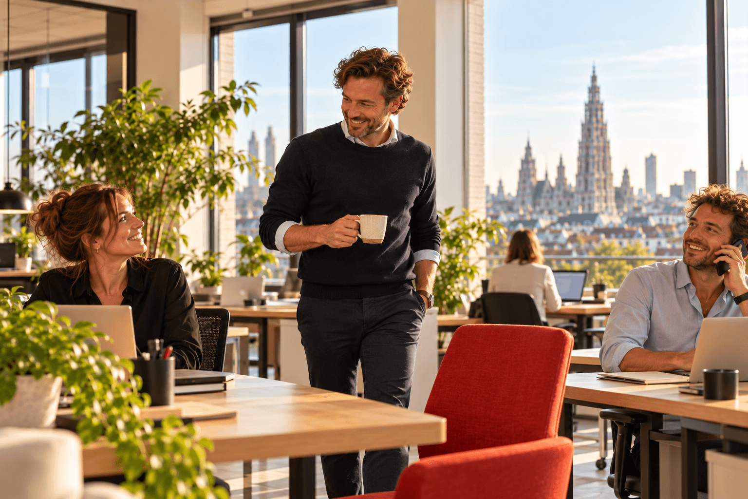 Recruiter stapt lachend met een koffie de salesvloer op en collega's begroeten hem, met de kathedraal van Antwerpen in de verte