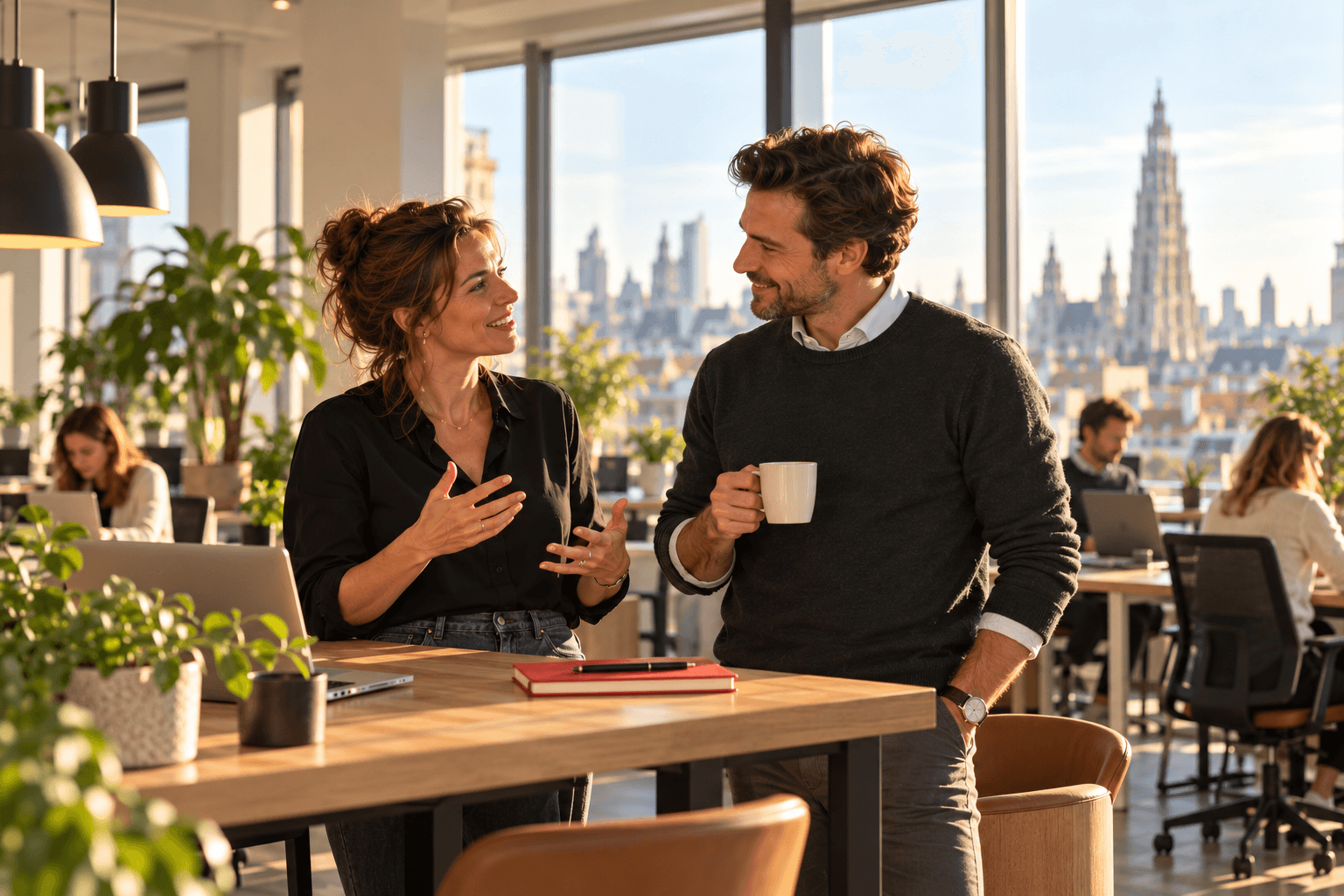 Twee recruiters in gesprek aan een hoge tafel op een lichte salesvloer, met de kathedraal van Antwerpen in de verte